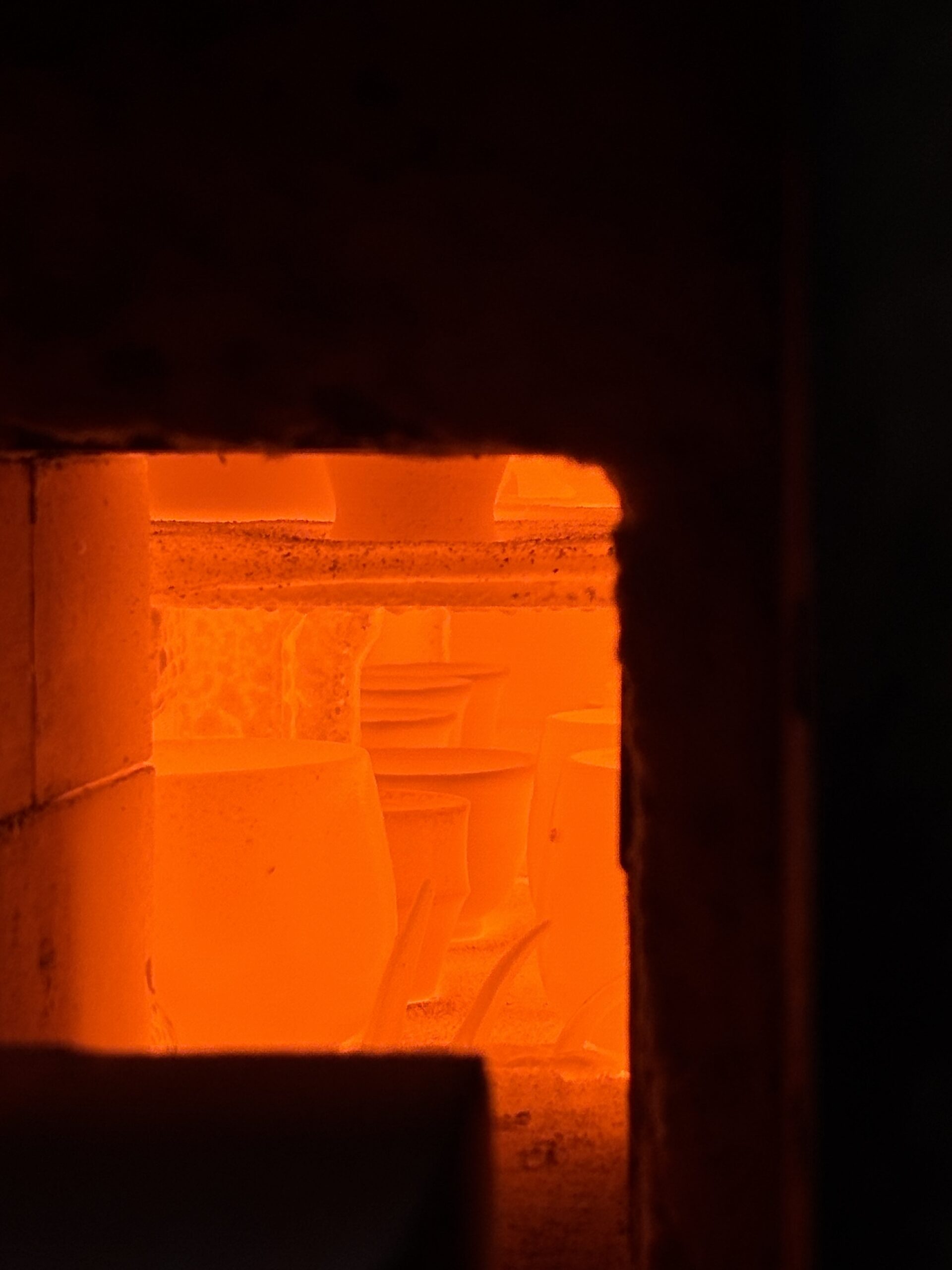 Interior view of a glowing orange ceramic kiln, showing the intense heat and flame during the 1300°C firing process for stoneware vases.