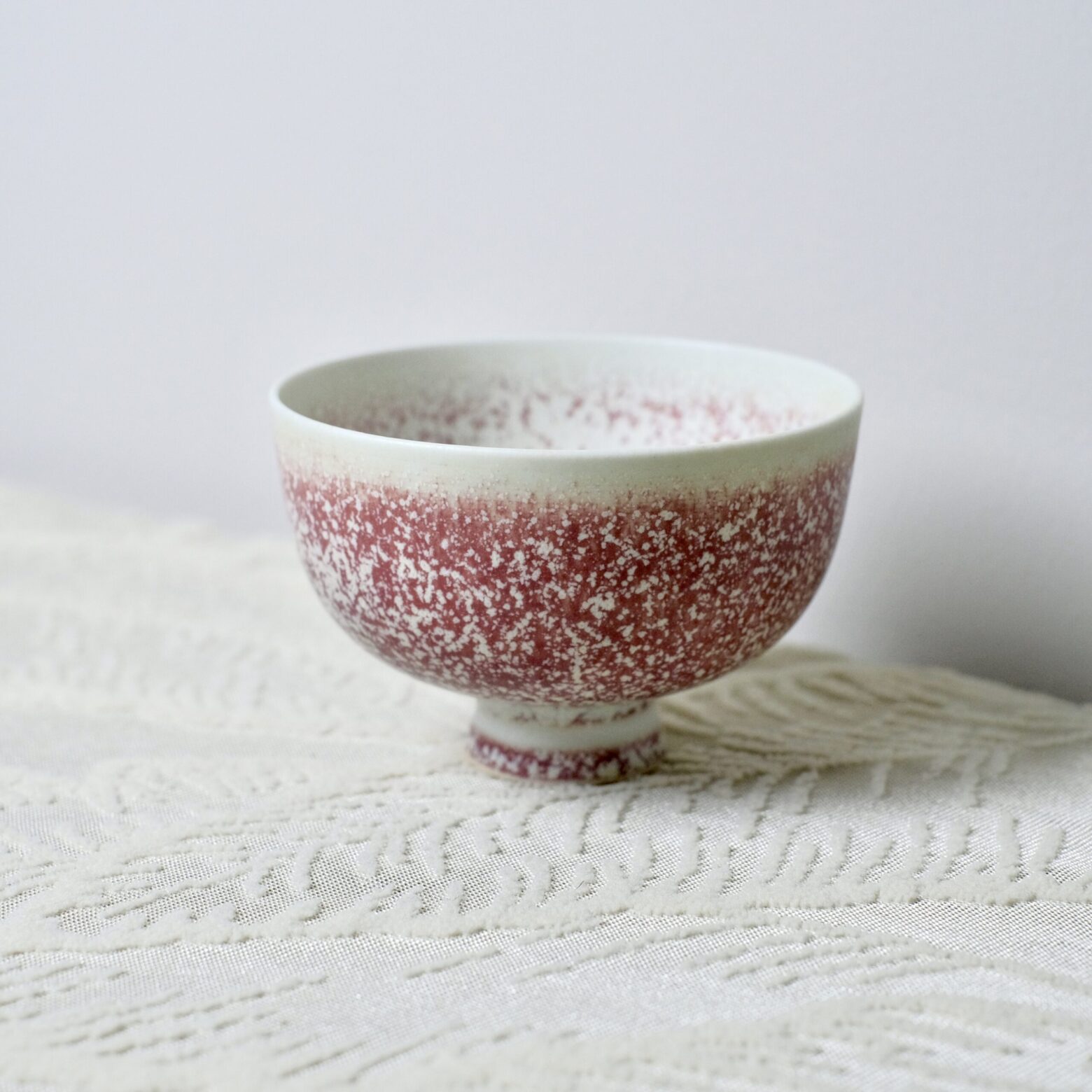 Artisan handmade ceramic tea bowl with red glaze in natural light setting, Yunnan pottery
