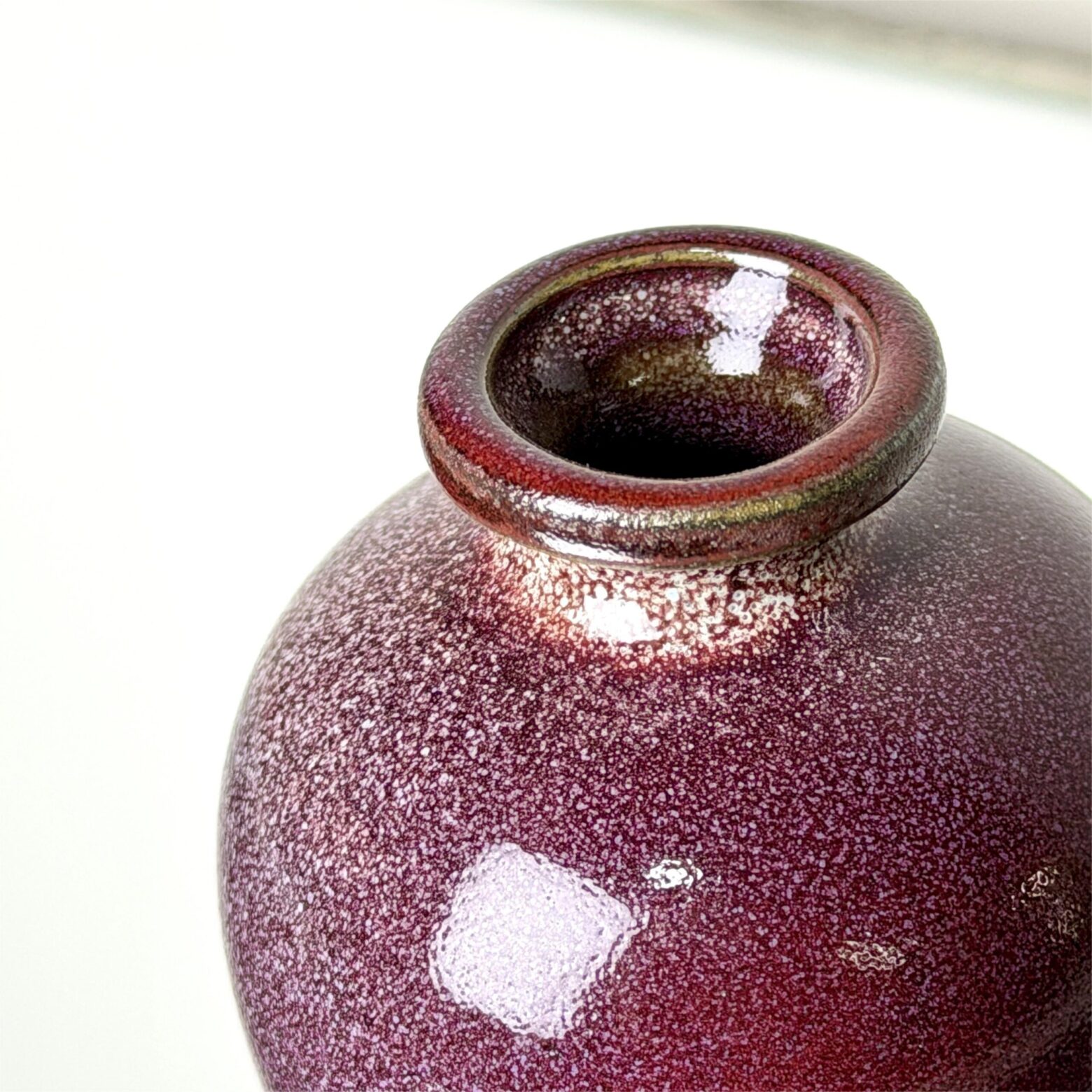 Close-up of handmade ceramic vase with red crystalline glaze and rounded rim, Yunnan pottery